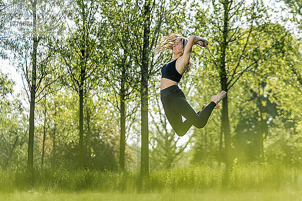 Glückliche Frau springt an einem sonnigen Tag im Park