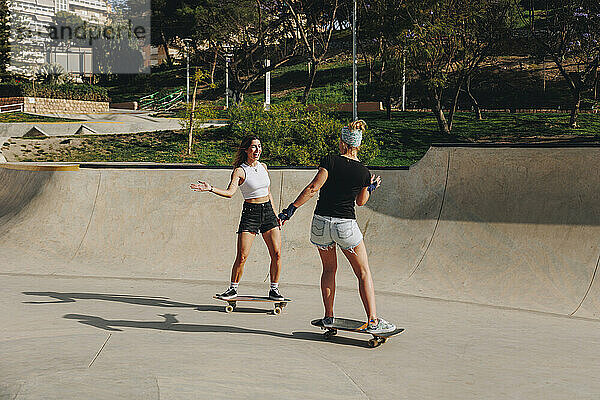 Glückliche Frauen  die an einem sonnigen Tag Skateboarden auf der Sportrampe genießen
