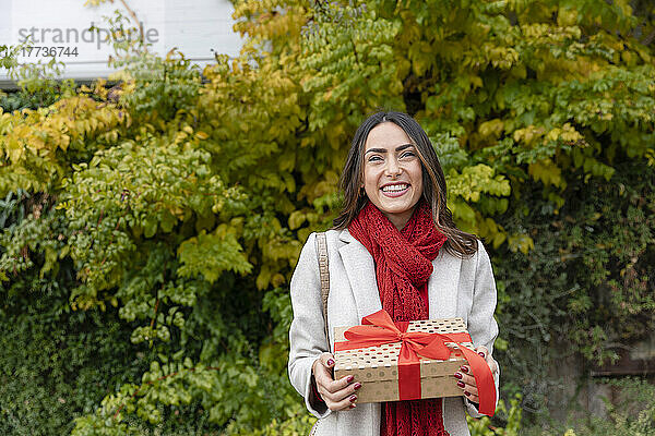 Glückliche schöne Frau mit Weihnachtsgeschenk steht im Park