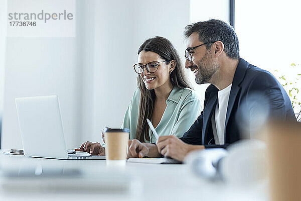 Lächelnde Geschäftsfrau und Geschäftsmann diskutieren am Laptop am Schreibtisch im Büro