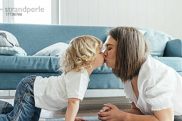 Zärtliche Mutter und Sohn mit geschlossenen Augen küssen sich auf dem Sofa zu Hause auf den Mund