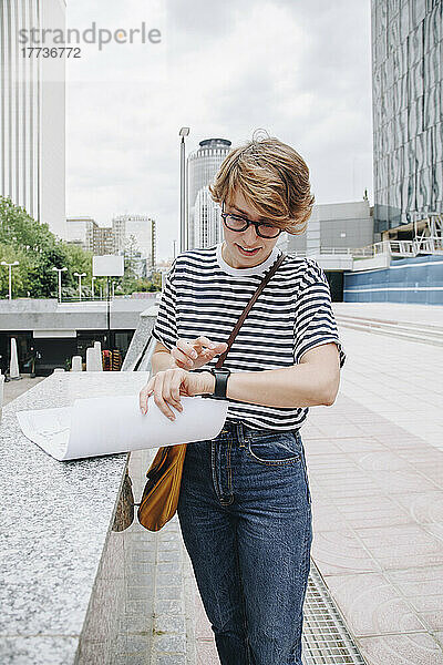 Geschäftsfrau steht mit Smartwatch in der Nähe der Mauer in der Stadt