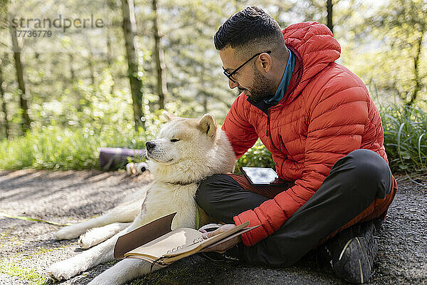 Mann mit Brille sitzt mit Hund im Wald