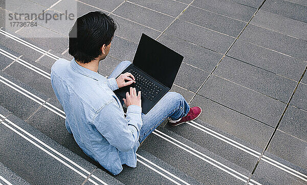 Mann benutzt Laptop und sitzt auf Stufen