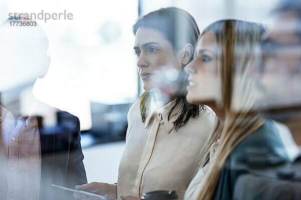 Geschäftsfrauen und Geschäftsleute diskutieren bei einem Treffen  gesehen durch Glas im Büro