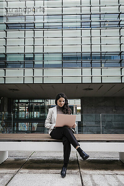 Engagierte junge Geschäftsfrau sitzt mit Laptop auf einer Bank