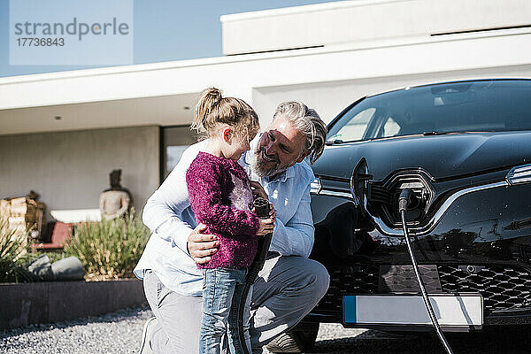 Glücklicher Mann mit Tochter  die einen Stromstecker vor dem Auto hält