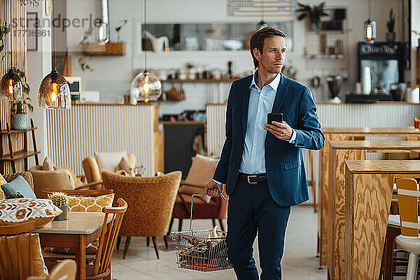 Reifer Geschäftsmann mit Gemüsekorb und Smartphone im Café