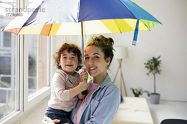 Mutter und Tochter stehen zu Hause und halten einen Regenschirm