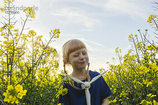 Glückliches Mädchen mit Windturbinenmodell inmitten von Pflanzen auf einem Rapsfeld