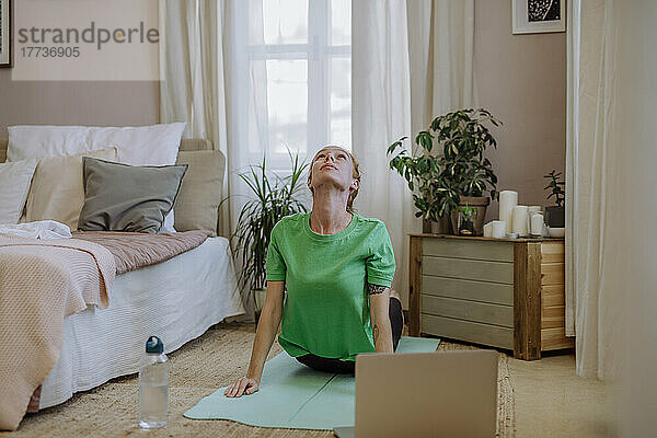 Frau praktiziert zu Hause Yoga-E-Learning über Laptop