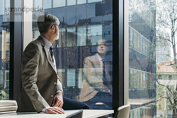 Geschäftsmann sitzt am Schreibtisch und blickt durch das Fenster im Büro