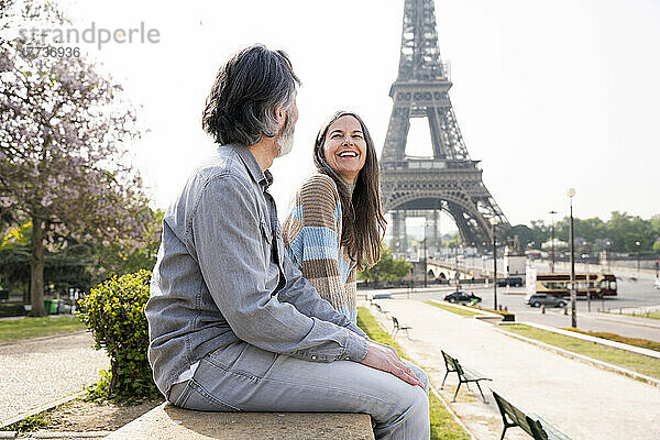 Fröhliche reife Frau sitzt mit ihrem Freund an der Wand vor dem Eiffelturm  Paris  Frankreich