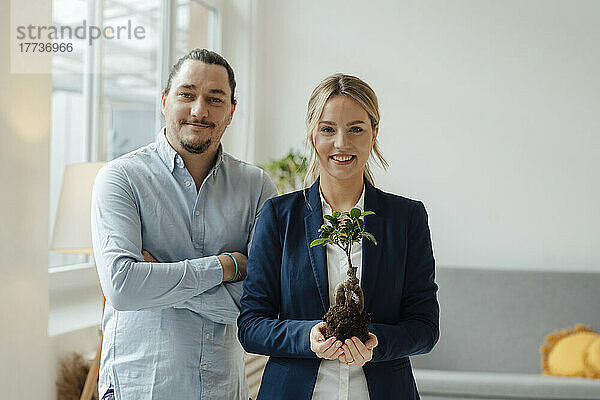 Lächelnde Geschäftsfrau  die Pflanze von einem Kollegen im Büro hält