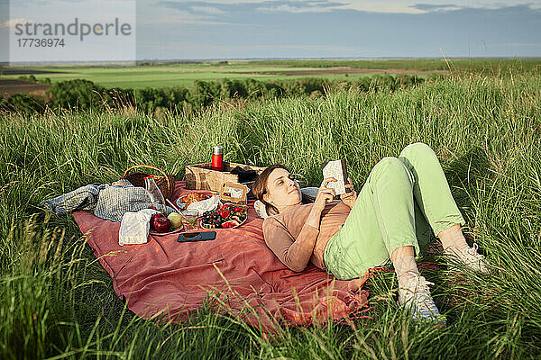 Lächelnde Frau liest Buch beim Picknick im Feld
