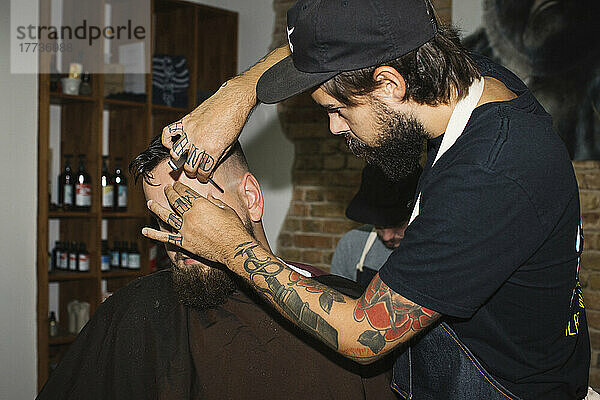 Mann im Friseurladen lässt sich den Bart mit einer Rasierklinge rasieren