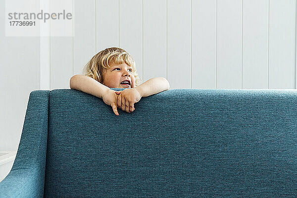 Cute boy standing behind sofa in living room at home