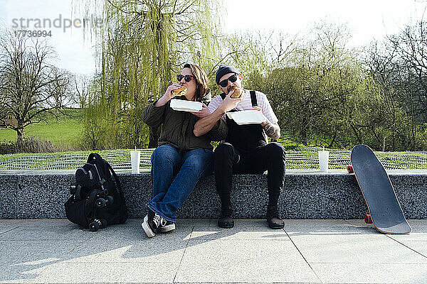 Freunde essen Burger auf dem Skateboard im Park