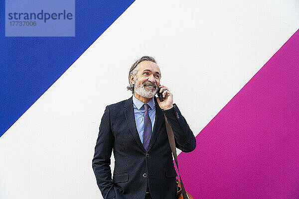 Glücklicher reifer Geschäftsmann  der vor einer bunten Wand mit dem Handy spricht