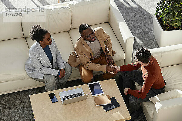 Geschäftsleute schütteln sich die Hand und sitzen mit Kollegen auf dem Sofa im modernen Büro