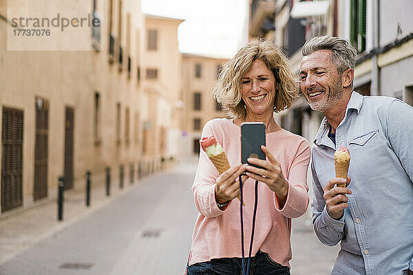 Glückliches Paar mit Eis  das in der Stadt ein Selfie mit dem Smartphone macht