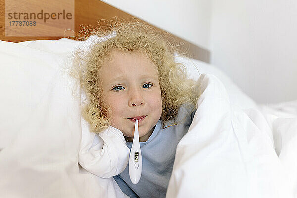 Girl with thermometer in mouth lying on bed at home