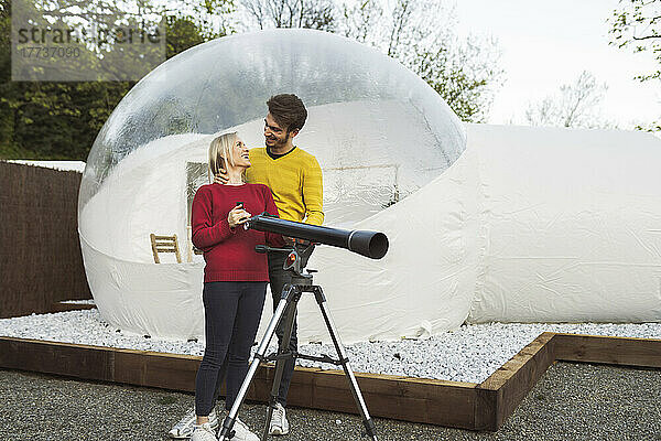 Glückliches Paar mit Teleskop vor transparentem Kuppelhotel