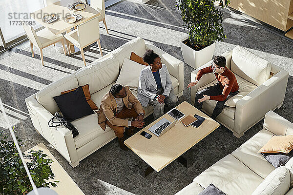 Junge Geschäftsleute und Geschäftsfrau diskutieren auf dem Sofa im modernen Büro über Strategie