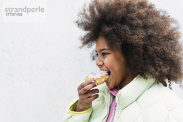 Afro-Mädchen mit lockigem Haar isst Donut