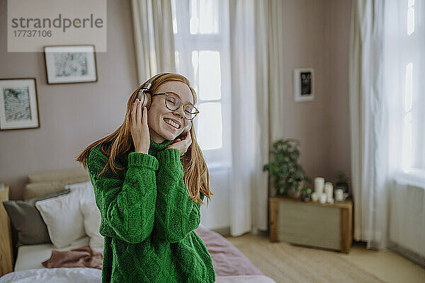 Glückliche Frau mit geschlossenen Augen  die zu Hause Musik über kabellose Kopfhörer genießt