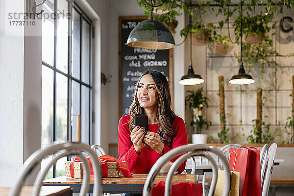 Lächelnde Frau sitzt mit Smartphone am Tisch im Café