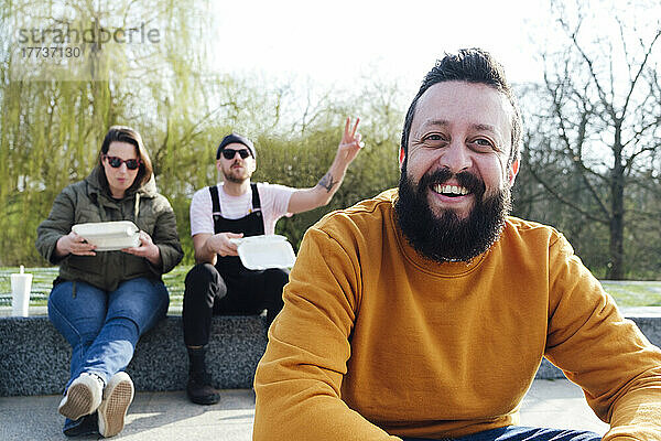Lächelnder Mann verbringt seine Freizeit mit Freunden im Hintergrund im Park