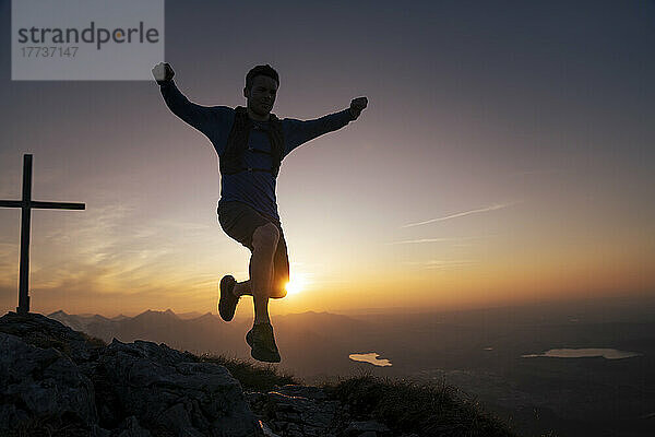 Wanderer springt bei Sonnenuntergang auf den Berggipfel