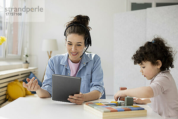 Mutter arbeitet von zu Hause aus mit digitalem Tablet  während Tochter mit Bauklötzen spielt