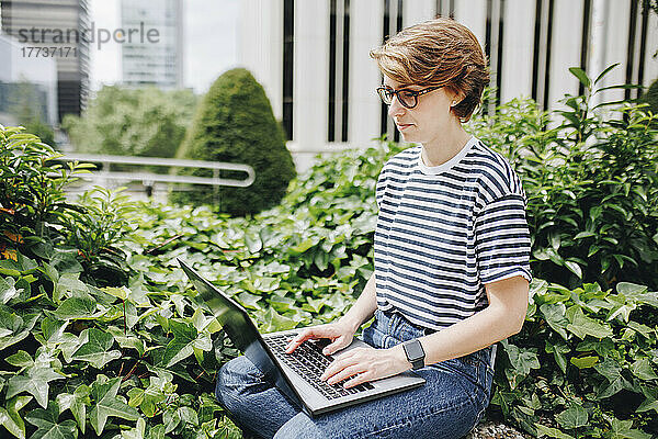 Frau arbeitet am Laptop und sitzt inmitten von Pflanzen