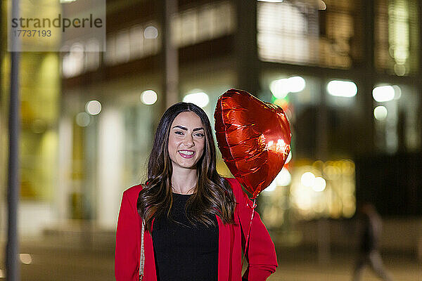 Lächelnde Frau hält nachts einen herzförmigen Ballon