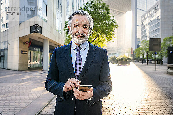 Lächelnder Geschäftsmann mit Smartphone steht im Büropark
