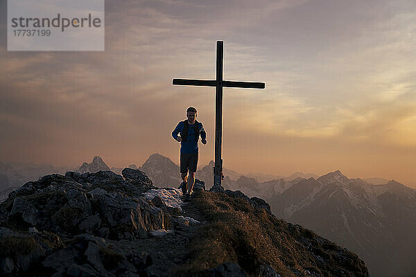 Wanderer läuft auf dem Sauling-Berggipfel mit Gipfelkreuz