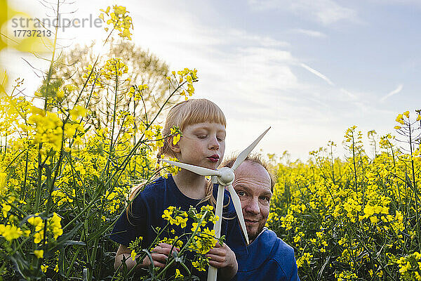 Lächelnder Vater mit Tochter bläst auf Windturbinenmodell auf Rapsfeld