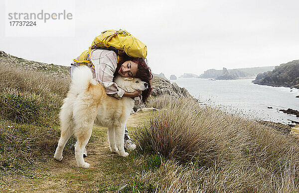 Lächelnde Frau mit Rucksack umarmt Hund