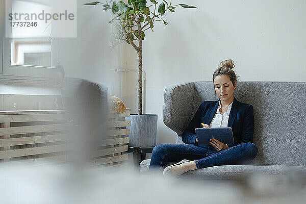 Geschäftsfrau sitzt mit Tablet-PC auf dem Sofa im Büro