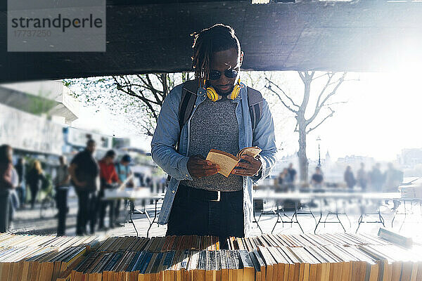 Junger Mann liest an einem sonnigen Tag ein Buch auf dem Straßenmarkt