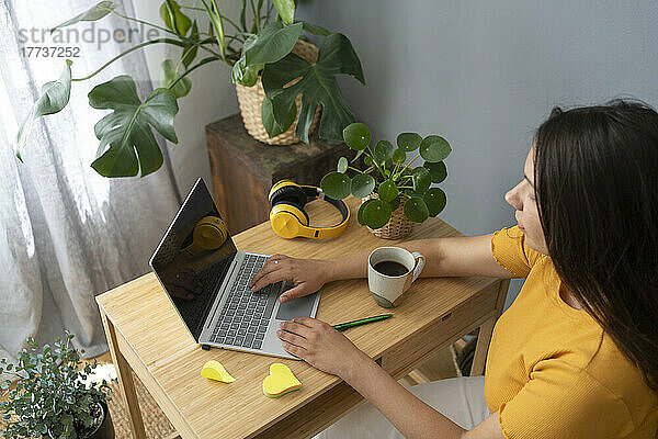 Frau mit Kaffeetasse und Laptop am Schreibtisch im Heimbüro