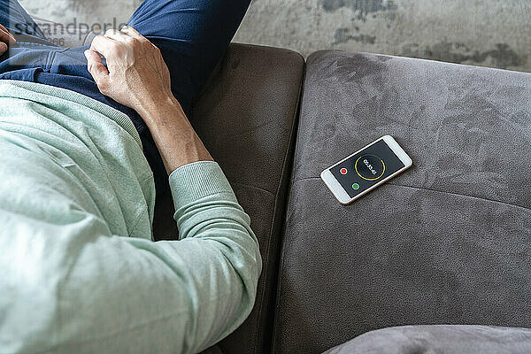 Mobile phone with timer by man sitting on sofa at home