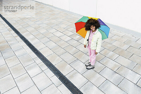 Mädchen mit buntem Regenschirm steht auf Fußweg
