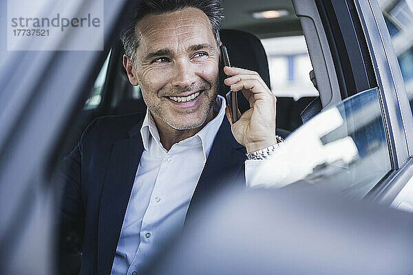 Glücklicher Geschäftsmann  der im Auto mit dem Handy spricht