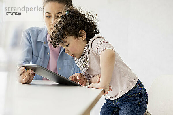 Kleines Mädchen schaut auf ein digitales Tablet  das von der Mutter gehalten wird