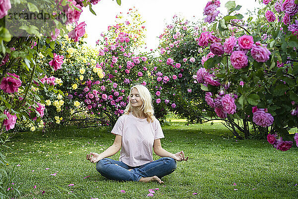Frau mit geschlossenen Augen meditiert inmitten eines Rosengartens
