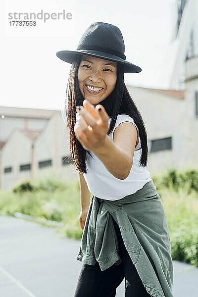 Fröhliche junge Frau mit Hut gestikuliert und genießt den Tanz an einem sonnigen Tag