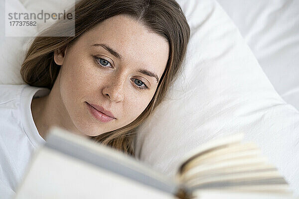Schöne Frau liest ein Buch  das zu Hause im Bett liegt